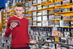 Handsome focused guy looking on box of DVD movie during shopping in CD shop