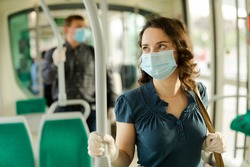 Portrait of female passenger in disposable medical mask and rubber gloves holding on handrails in urban bus. Concept of forced city trip in context of coronavirus pandemic