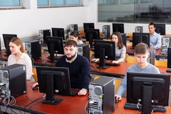 Group of smiling concentrated people of different ages learning to use computers in classroom