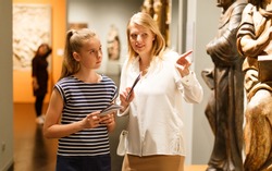 Young woman visitor with daughter with guide book looking at exhibition in museum of ancient sculpture