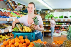 Cheerful positive smiling woman standing with full shopping cart during shopping in fruit store