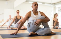 Latin american man practicing Matsyendrasana known as Lord of Fishes Pose during group yoga training