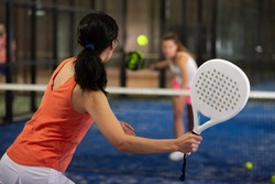 Rear view of brunette girl with white racket playing padel tennis at court