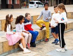 Cheerful multiethnic group of tweens spending time together on city street in warm fall day .
