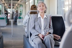 Mature woman with handbag sitting on seat inside tram.