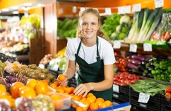 Cheerful young girl employees in uniform holding fresh mandarines in grocery shop