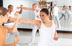 Young Hispanic woman paired up with female partner in self defense training, practicing basic moves of close combat