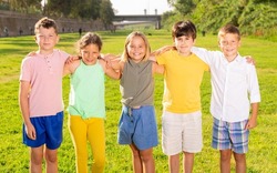 Group photo of friendly children standing on grass in field.