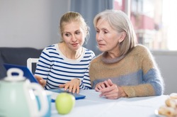 Elderly mother and adult daughter looking at laptop screen at home