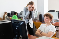 Female teacher amazed by misbehavior of her student, teenage boy, during computer science lesson.