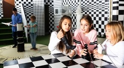 Portrait of focused tween girls trying to solve conundrum in quest room stylized under chessboard