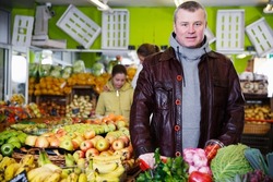Portrait of smiling young man with full shopping cart in fruit market