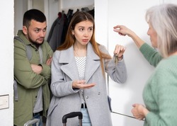 Dissatisfied old woman, owner of apartment, receiving keys from married couple tenants.