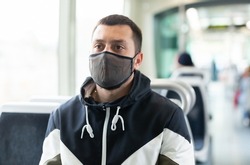Young man wearing protective face mask sitting in modern streetcar on sunny spring day during COVID-19 virus pandemic. Forced precautions in public transport