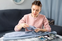 Young woman sitting at table at home and stitching clothes.