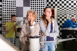 Grandmother and granddaughter thinking about solution of conundrum while standing in escape room. Young boy and grandfather working on conundrums in background..