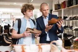 Shoe store employee helping teen to choose classic brown shoes in a shoe store