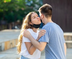 Young man and girl in masks are hugging and kissing each other in cheek