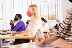 Young woman in protective face mask listening to lesson in extension school. Concept of necessary precautions and social distancing in coronavirus pandemic..