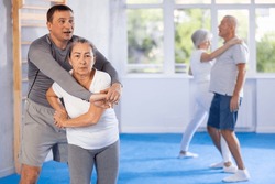 In gym female pensioner work out skill at sparring bout and perform basic elements of krav maga self-defense system. Preparation of athletes before competitions