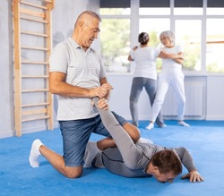 In gym male pensioner work out skill at sparring bout and perform basic elements of krav maga self-defense system. Preparation of athletes before competitions