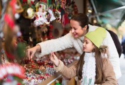 Smiling mother with positive girl in Christmas market. Focus on girl