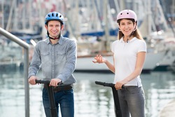 Young couple driving a segways along sea front and smiling. Focus on both persons 