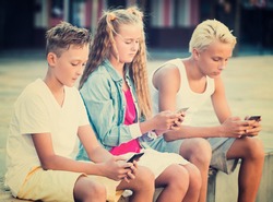 Modern kids spending time together outdoors using mobile gadgets