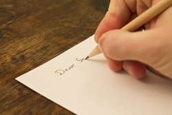 A close photo of a persons writing a letter with a pencil.