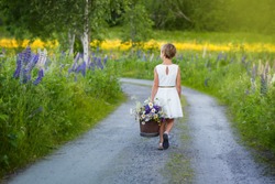 Girl with a bucket of flowers walking on a dirt road
