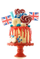 UK on-trend candyland fantasy drip cake with red, white and blue decorations, lollipops and flags on white background.