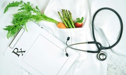 Healthy lifestyle, food is medicine, concept flatlay with fruit and vegetables in pocket of white doctor's coat with clipboard and stethoscope.