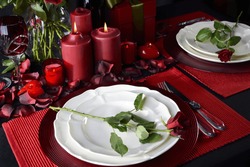 Romantic Valentine Candle Light Dinner for Two Table Setting for two with red roses, gift and burning candles against a black background. 