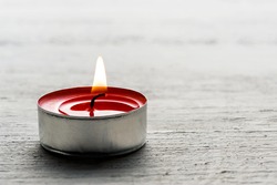 Close up of a single burning red tea light candle in a metal base on a white textured background with copy space for your message or invitation