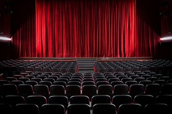 Darkened empty movie theatre and stage with the red curtains drawn viewed over rows of vacant seats from the rear