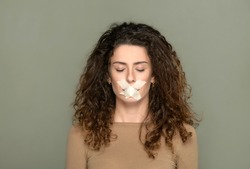 Young woman with closed eyes and her mouth taped shut in a concept of censorship of vision and free speech over a grey studio background
