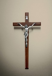 Wooden crucifix with metal Jesus Christ figure for prayer hanging on beige wall