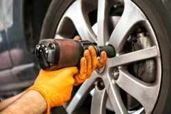 Mechanic working on a car wheel tightening or loosening the bolts on the hub and rim with an electric power tool, close up view of his hands