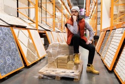 a customer in a hardware store sits on a pallet with ceramic tiles pensive pose