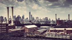 CITYSCAPE FROM BROOKLYN WITH OLD FACTORIES AND CHIMNEYS WITH THE SKYLINE OF NEW YORK CITY AND THE BROOKLYN BRIDGE IN THE BACKGROUND. VINTAGE COLOURS LIKE RED AND BROWN, PANORAMA VIEW ,CLOUDED BLUE SKY