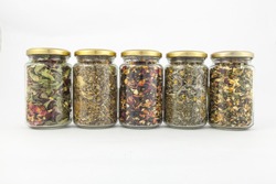 A range of transparent glass jars of different herbs.
