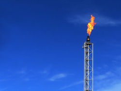 Gas flare is releasing and burning to the atmosphere at an offshore gas platform with sky. Fire on a stack of flare at oil and gas central processing platform. A gas flare at an oil refinery.	
