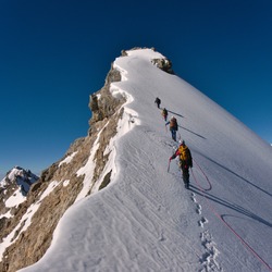 Tied climbers climbing mountain with snow field tied with a rope with ice axes and helmets