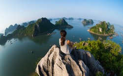 A young traveler girl sit on the top of mountain in Halong bay and enjoy the beauty of seascape. Young girl love wild life, travel, freedom.