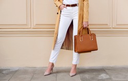 Closeup female legs. Woman in coat and white jeans with brown handbag. Fashion street autumn outfit