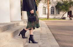 woman pose in black ankle boots with mini bag on the stairs, street style outfit