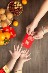 Chinese lunar new year flat lay traditional food and offering on table top. Senior women hands giving red packet to toddler boy hands.