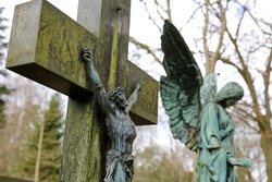 
Old Crucifix in a graveyard, Jesus on the cross. Green bronze angel statue in the background.