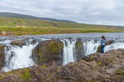 A woman looking at Kolufoss waterfall at Kolugljufur canyon on Iceland
