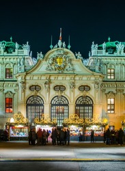 People are buying various articles during a christmas market during night taking place in front of the belvedere palace in vienna.